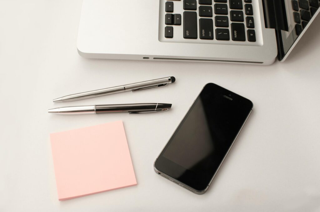 Clean and modern workspace featuring a laptop, smartphone, pens, and sticky notes.